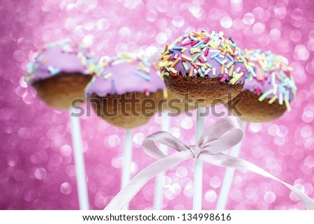 Pink cake pops decorated with colorful sprinkles. Pink glittering background, very festive.