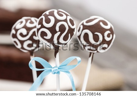 Chocolate cake pops decorated with white icing. Chocolate cake on wooden table in the background. Selective focus.