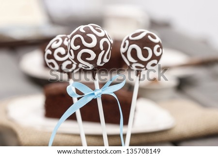 Chocolate cake pops decorated with white icing. Chocolate cake on wooden table in the background. Selective focus.