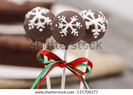 Chocolate cake pops decorated with white icing. Brown chocolate cake on wooden table in the background.