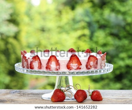 Strawberry cake on wooden table in lush summer garden