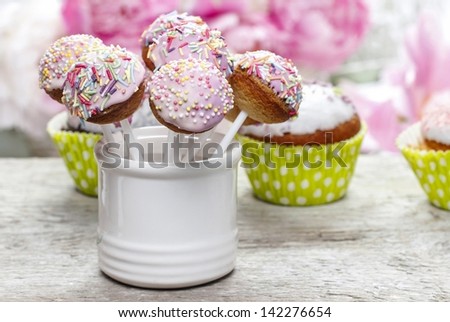 Pastel cake pops and cupcakes on rustic wooden table. Stunning peony flowers in the background.