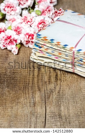 Package of old letters and pink carnation flowers isolated on wooden background. Copy space.