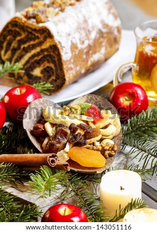 Candles, apples, dried fruits, fir branches and poppy seed cake on christmas eve table