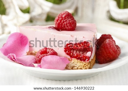 Piece of raspberry cake decorated with fresh fruits and rose petals. Romantic setting