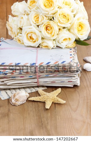 Stack of old letters and bouquet of pastel yellow roses on wooden table. Romantic vintage setting. Copy space