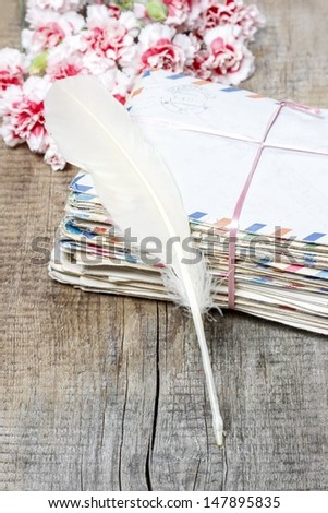 Stack of old letters, feather pen and bouquet of pink carnations on wooden table
