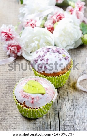 Delicious muffins with icing on wooden table. White peonies in the background.