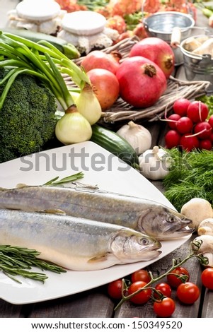 Two raw, fresh rainbow trouts among vegetables. Idea of healthy living and valuable, natural food.