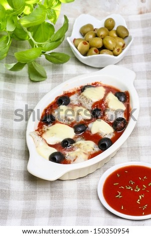 Cheese, tomato sauce and black olives gratin on checkered table cloth. Basil plant in the background.