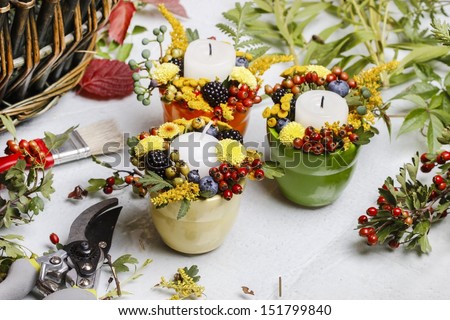Candle holder decorated with autumn flowers and other plants. Making floral decorations at florist workshop.
