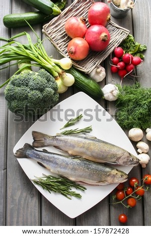 Top view on huge wooden table: two raw, fresh rainbow trouts among vegetables. Idea of healthy living and valuable, natural food.