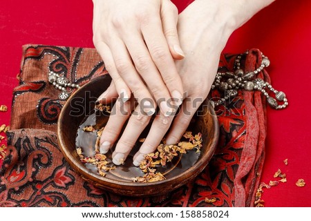 Woman in a nail salon receiving a manicure, she is bathing her hands in water with rose petals