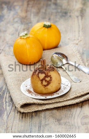 Baked apple decorated with cinnamon heart shape ornament. Pumpkins in the background. Autumn mood.