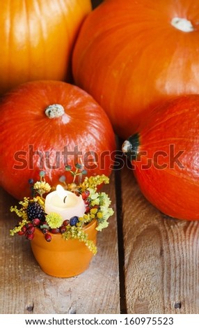 Orange candle holder decorated with autumn flowers and other plants among ripe pumpkins on wooden table.