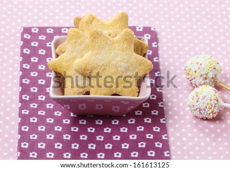 Cookies in star shape and white cake pops decorated with colorful sprinkles on dotted table cloth.