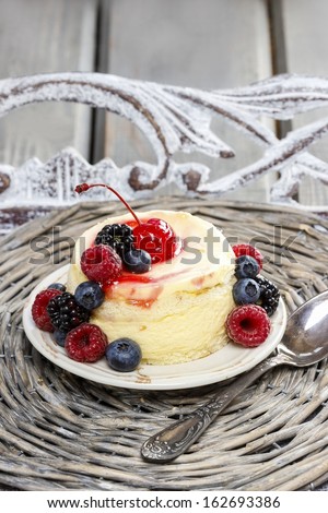Round vanilla cake decorated with fresh fruits: cherries, blueberries, blackberries and raspberries. Yummy dessert on wicker tray.