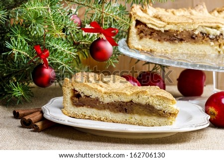 Apple pie in christmas setting. Cake on wooden table, christmas tree in the background.