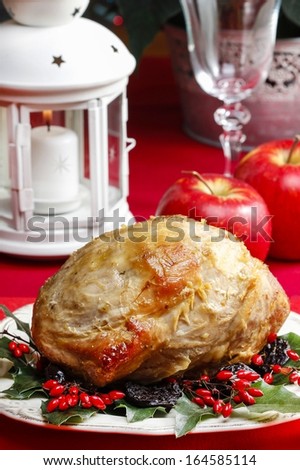 Baked pork with dried plums on christmas table. Apples and white lantern in the background