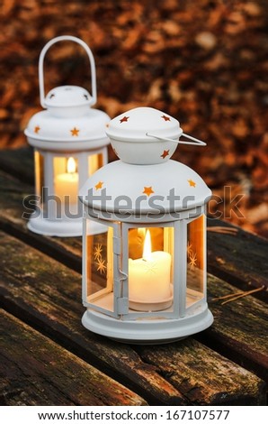 Two white lanterns on wooden bench. Autumn forest in the background