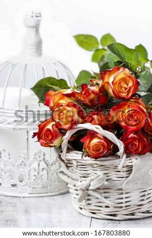 Basket of orange roses and white victorian birdcage on white background