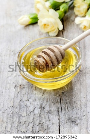 Bowl of honey and bouquet of yellow carnation flowers in the background