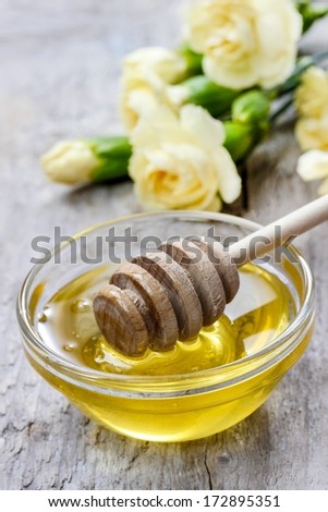 Bowl of honey and bouquet of yellow carnation flowers in the background