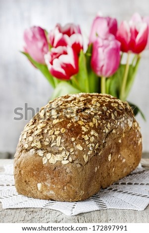 Loaf of bread. Bouquet of red and pink tulips in the background, copy space