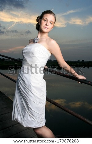 Beautiful young woman in a white summer dress dancing at the beach party. Pretty girl on wooden pier at sunset.