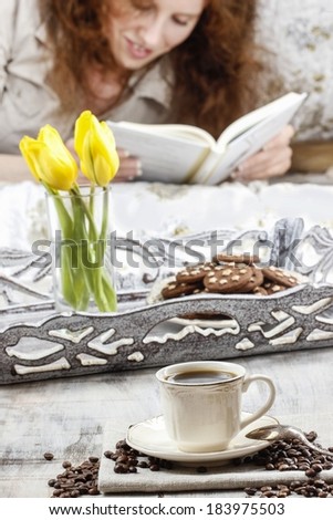 Time to relax: young woman enjoying reading a book, sitting on the sofa. Cup of coffee on the table.