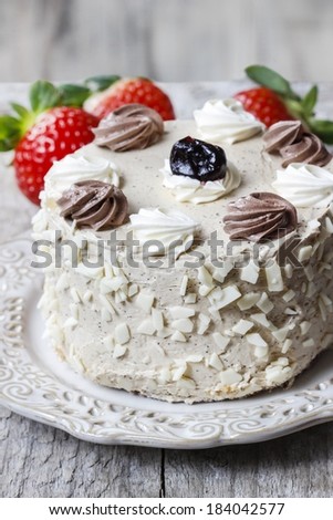 Round vanilla cake on cake stand. Fresh strawberries in the background.