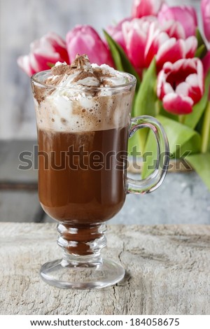 Irish coffee on wooden table. Bouquet of pink and red tulips in the background