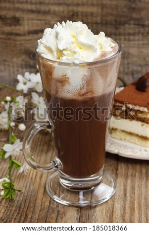 Irish coffee on wooden table. Tiramisu cake and blooming apple branch in the background