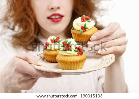 Eat or not to eat: woman hesitating over the plate with rose cupcakes