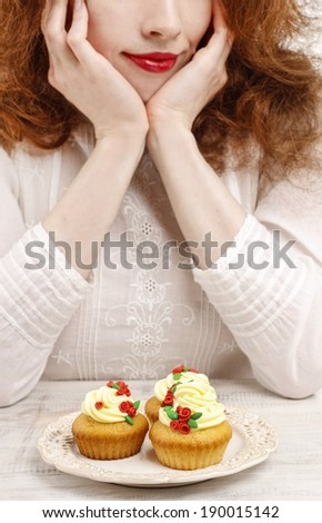 Eat or not to eat: woman hesitating over the plate with rose cupcakes