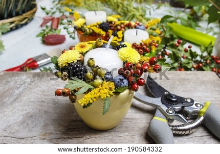 Candle holder decorated with autumn flowers and other plants. Making floral decorations at florist workshop.