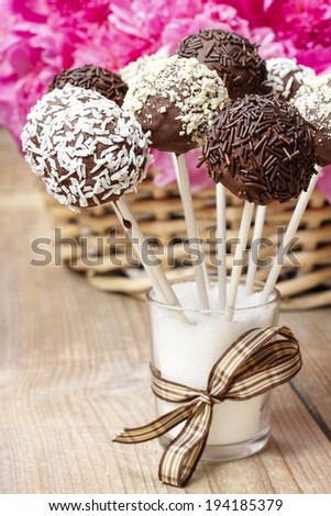Chocolate cake pops on wooden table. Basket of pink peonies in the background