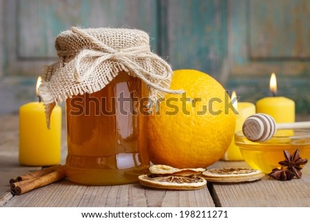 Jar of honey, oranges and candles on wooden table