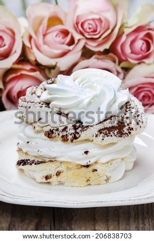 Meringue (pavlova cake) with cocoa. Bouquet of pink roses in the background