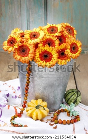 Bouquet of orange gerbera daisies in silver bucket on wooden table