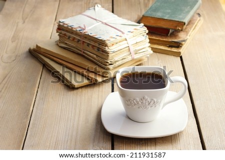 Cup of coffee on wooden table. Vintage books and pile of letters in the background
