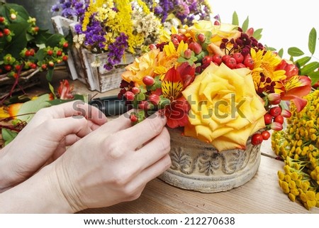 Florist at work: woman making bouquet of orange roses and autumn plants