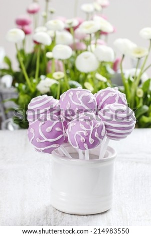 Lilac cake pops in white ceramic jar. White daisies in the background. Party table setting.