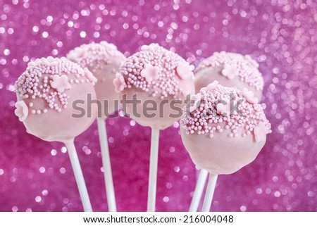 Pink cake pops decorated with sprinkles. Pink glittering background