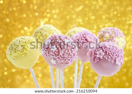 Pink and yellow cake pops decorated with sprinkles. Gold glittering background