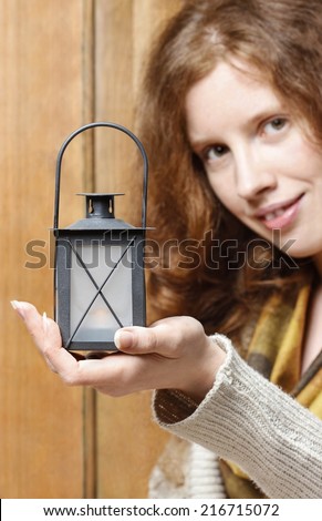 Woman holding christmas lantern. Wooden wall in the background