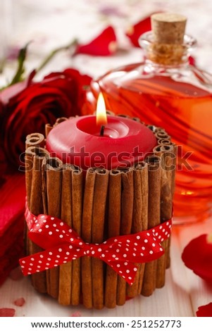 Red scented candle decorated with cinnamon sticks. Rose petals around.