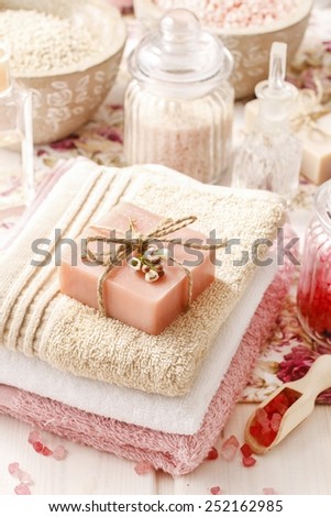 Bar of natural handmade soap lying on a towel, bottles of sea salts in the background
