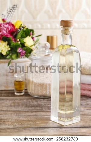 Bottle of essential oil and jar of sea salt on wooden table. Bouquet of flowers in the background