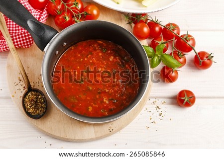 Red sauce made of dried tomatoes on frying pan. Wooden background, basil leaf and grains of pepper.